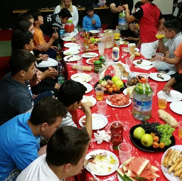 Gruppenspeisen an einem festlich gedeckten Tisch mit Kindern, frischem Obst und Getr&auml;nken in Bechern.
