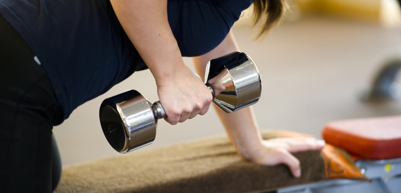 Frau macht eine Bizepsübung mit einer Hantel, während sie auf einer Trainingsbank lehnt.