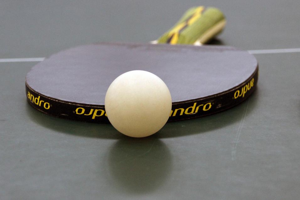 Nahaufnahme eines Tischtennisschlägers mit weißem Ball auf einer grünen Tischtennisplatte.