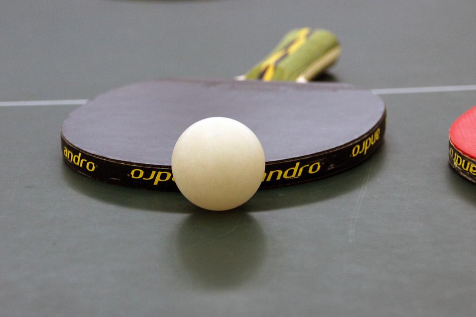 Nahaufnahme eines Tischtennisschlägers mit weißem Ball auf einer grünen Tischtennisplatte.